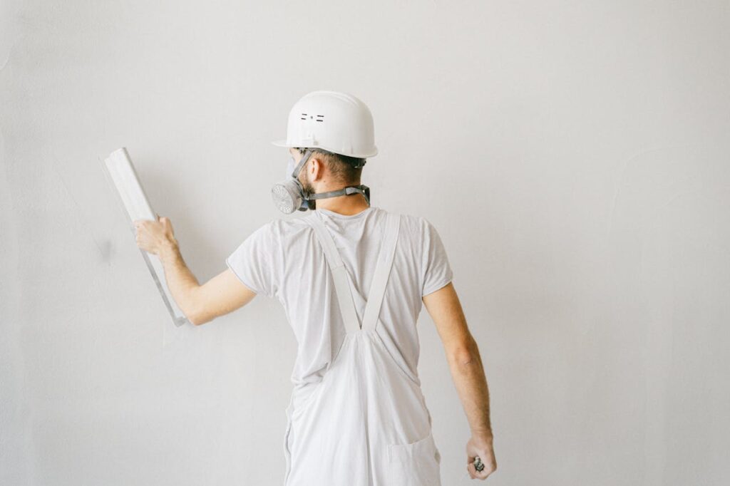 pexels-photo-5493658 Back view of a construction worker in safety gear plastering a white wall.
